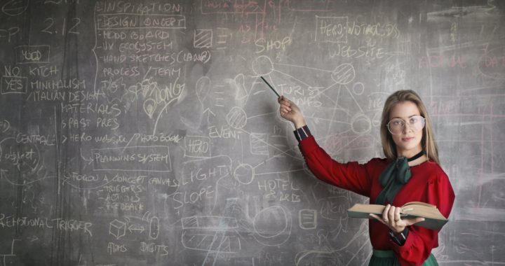 strict female teacher with book pointing at scribbled blackboard